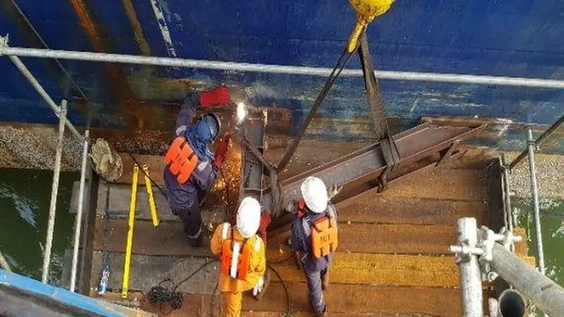 Marine repair crew working on a vessel deck alongside a moored jack-up boat